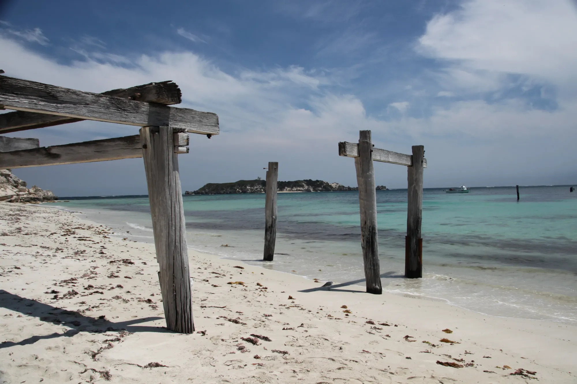 The weathered posts of an old jetty on a white Western Australian beach above clear shallow water